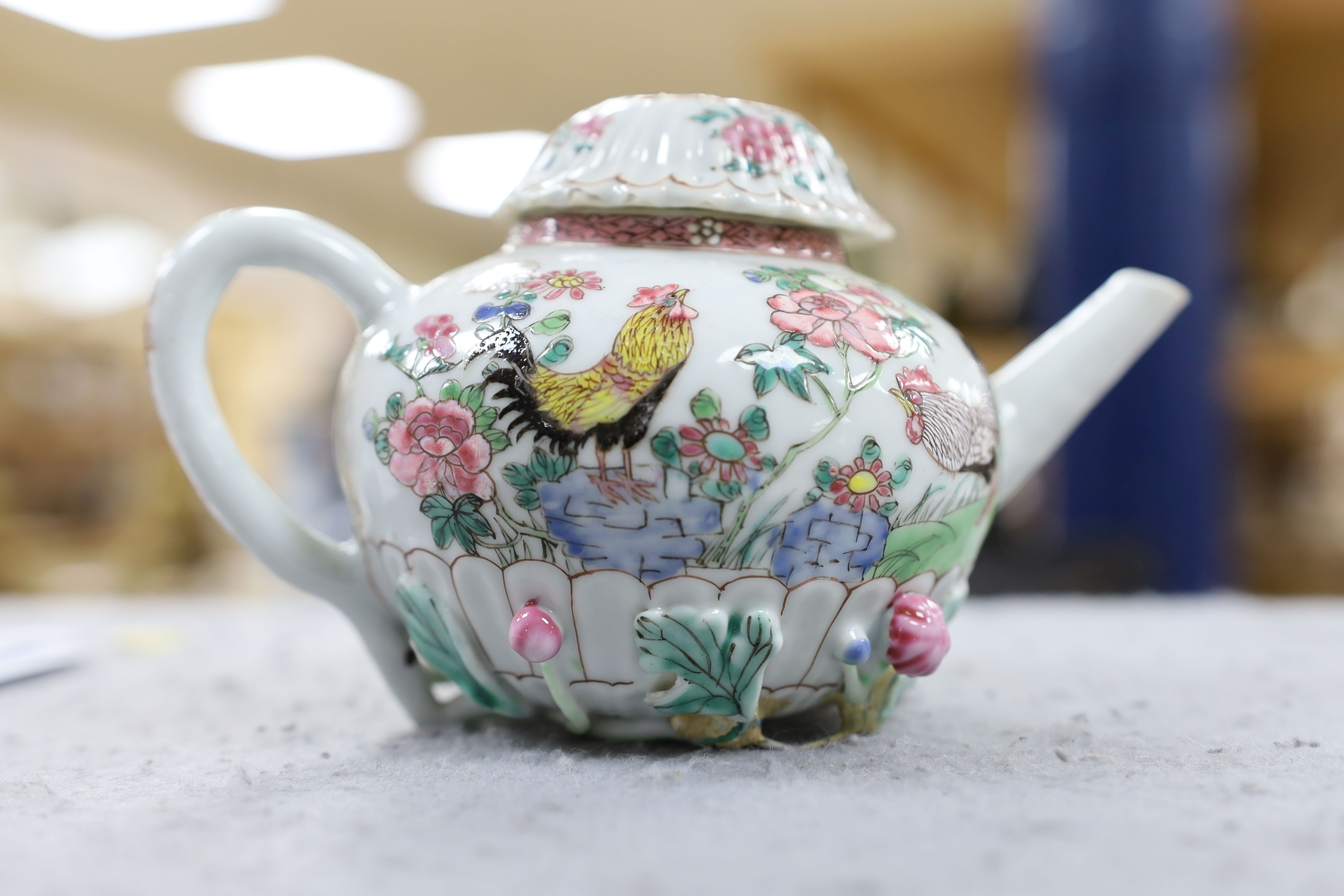 A Chinese famille rose chrysanthemum moulded teapot, early Qianlong period, painted with a cockerel amongst flowers, on a cage work base, 10 cms high